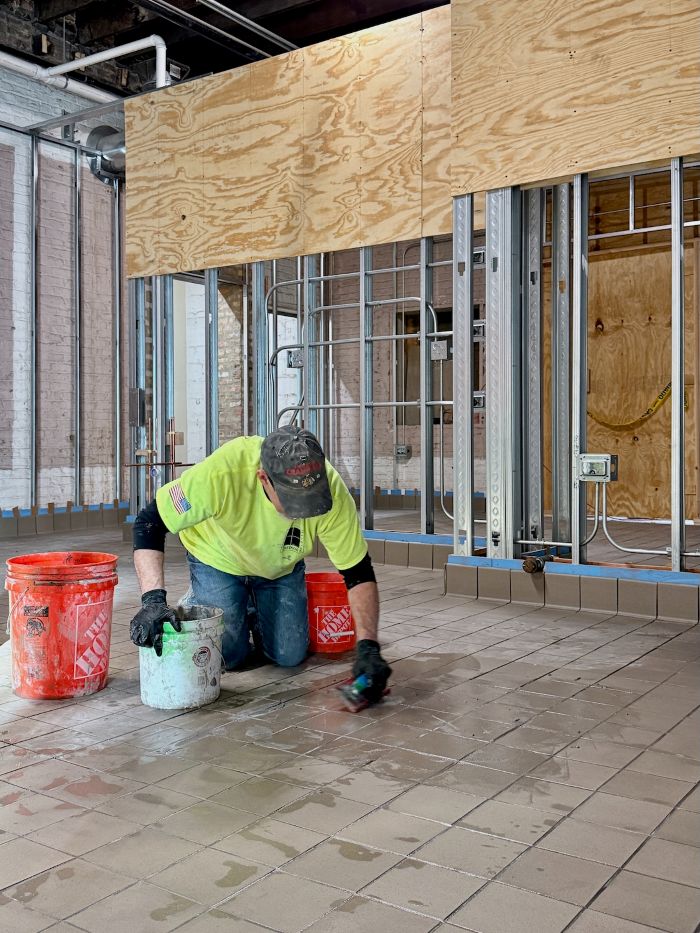 Commercial flooring installer in safety gear kneeling and working on tile or vinyl installation in a construction site